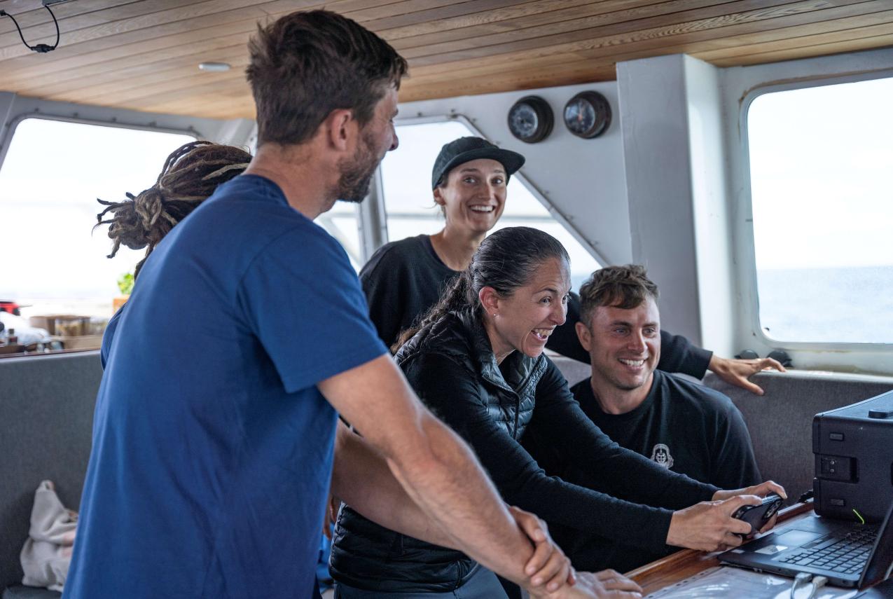 Five people on a boat looking at a computer
