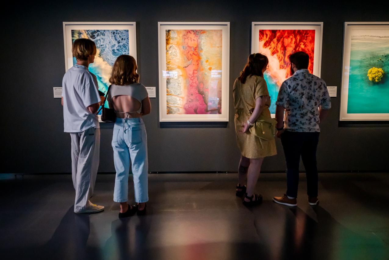 Four people look at a series of large, colourful landscape photographs presented on a gallery wall