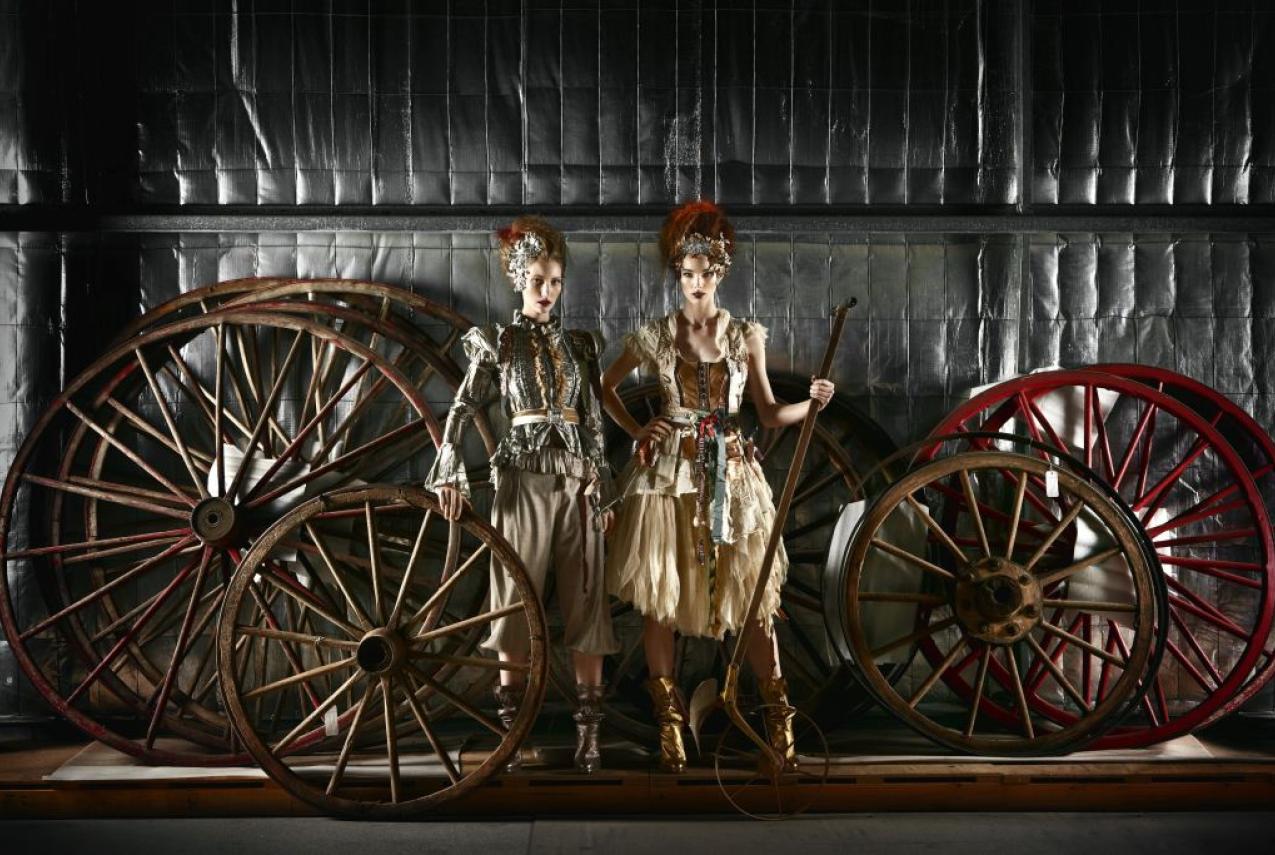 Two female models posing in front of large wheels
