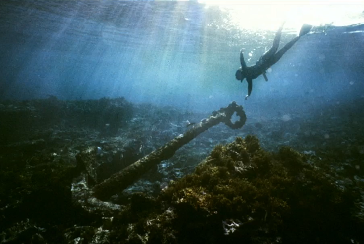 A snorkeler dives towards an anchor deep in the ocean.