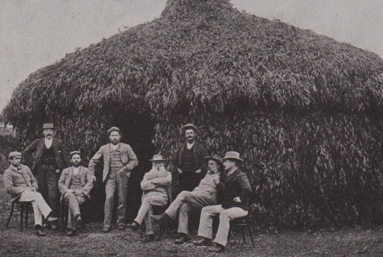 A crowd of people in front a large grass hut