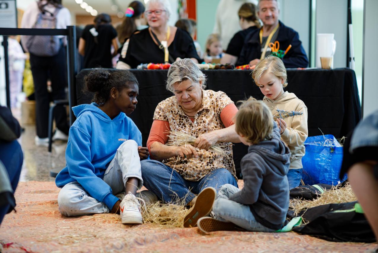 Women sitting with three children of varying age, demonstrating weaving.