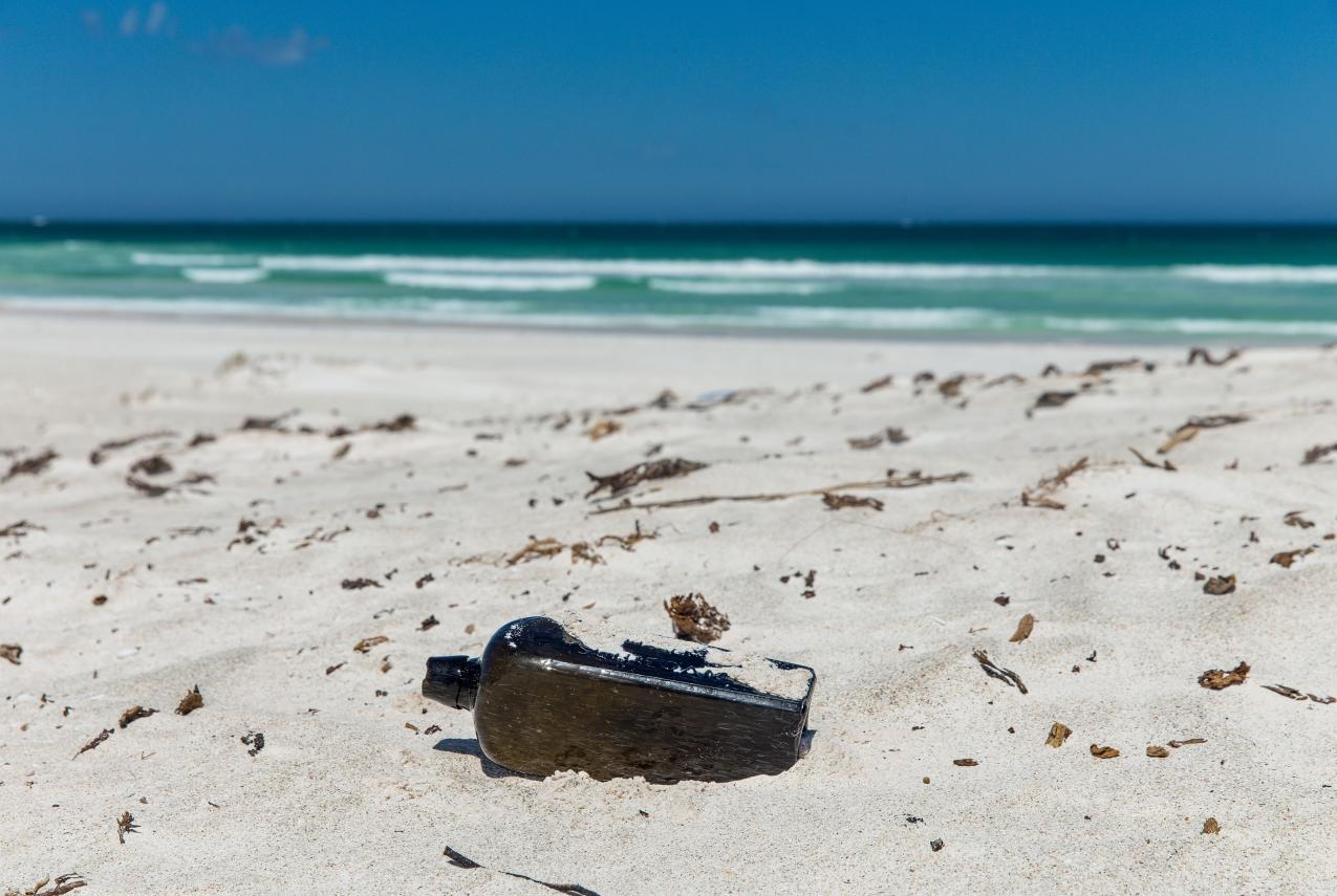 "The bottle is half submerged in sand in the foreground, with crashing waves in the background."