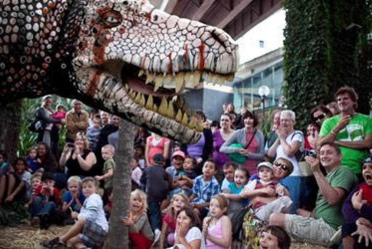 A massive dinosaur puppet meeting a crowd of children