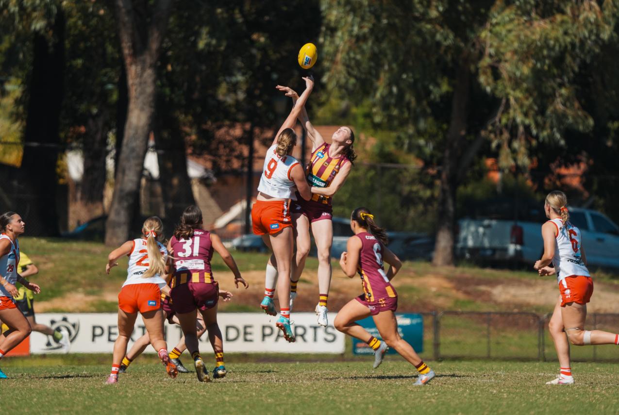 A group of female AFL players mid game, with two jumping high for a ball.