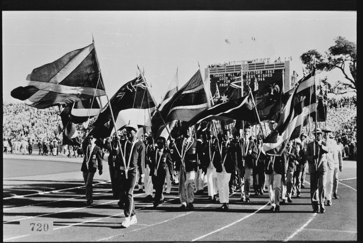 Black and white photograph of flag bearers marching on a track