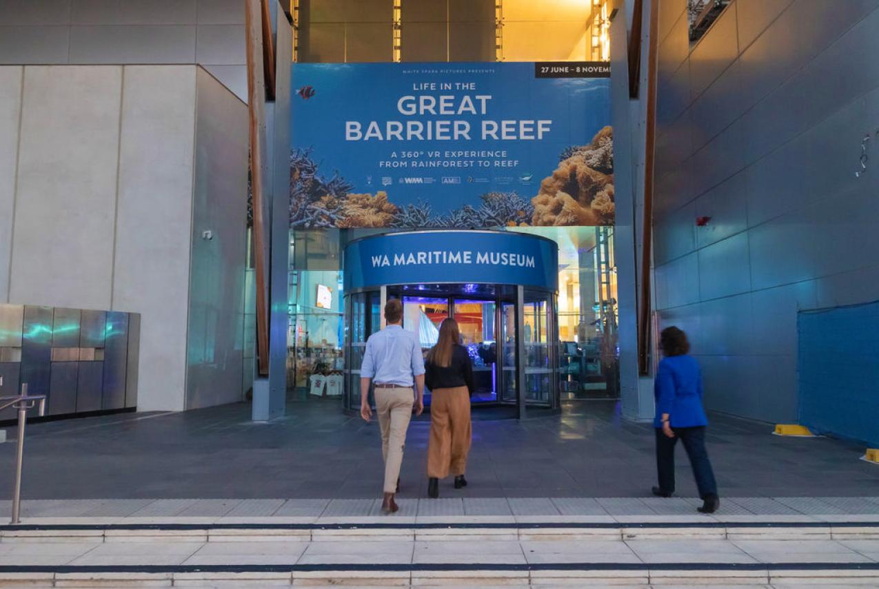 Three people walking to the entrance of the WA Maritime Museum, displaying advertising for Life in the Great Barrier Reef