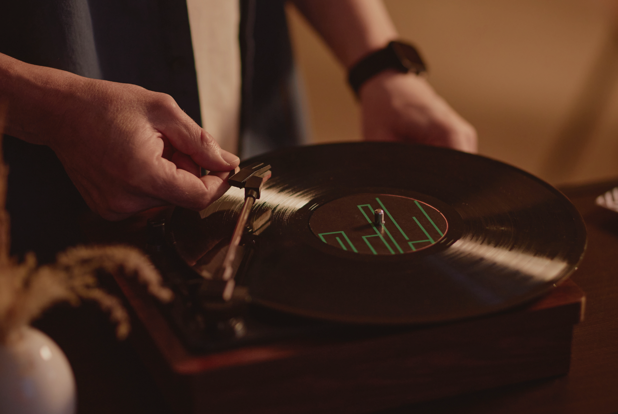 Close-up of a person placing a turntable needle onto a vinyl record on a wooden record player in warm indoor lighting.