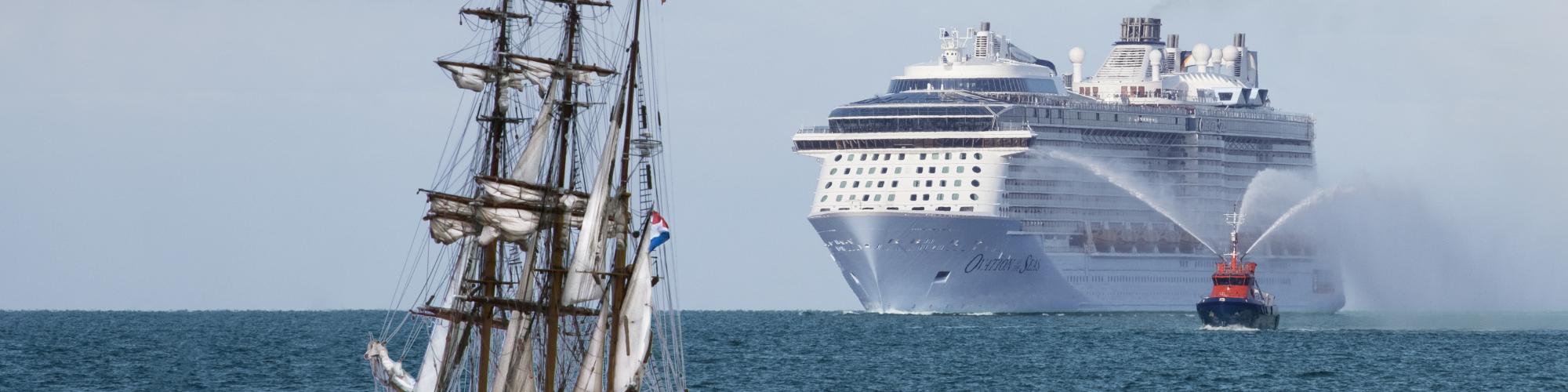 A masted ship sails on the open ocean in front of a modern ocean cruise liner