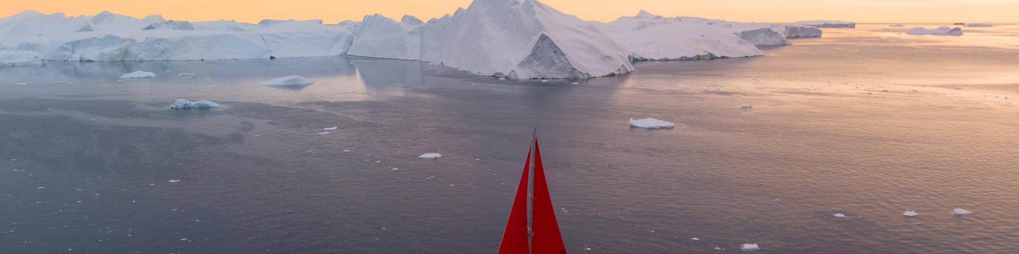 boat with red sails is sailing in water with icebergs in the background