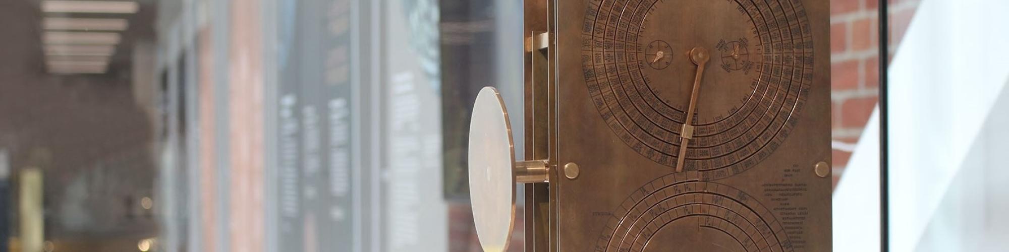 A brass model of the Antikythera mechanism displaying two dials with Greek characters, in a display cabinet