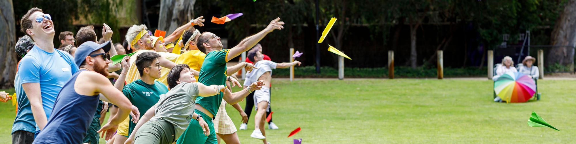 A group of people throwing colourful paper airplanes in a park.