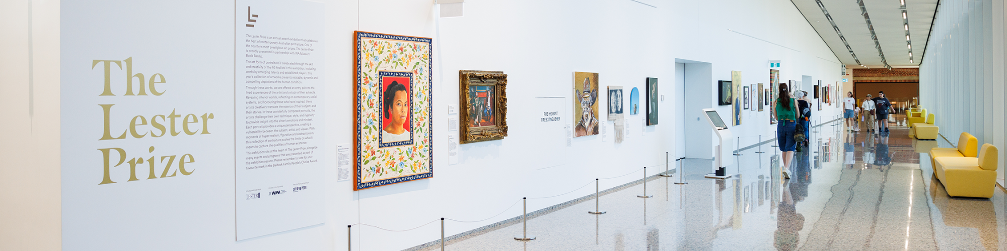 A modern museum corridor with "The Lester Prize" exhibition, showcasing various framed artworks on white walls.