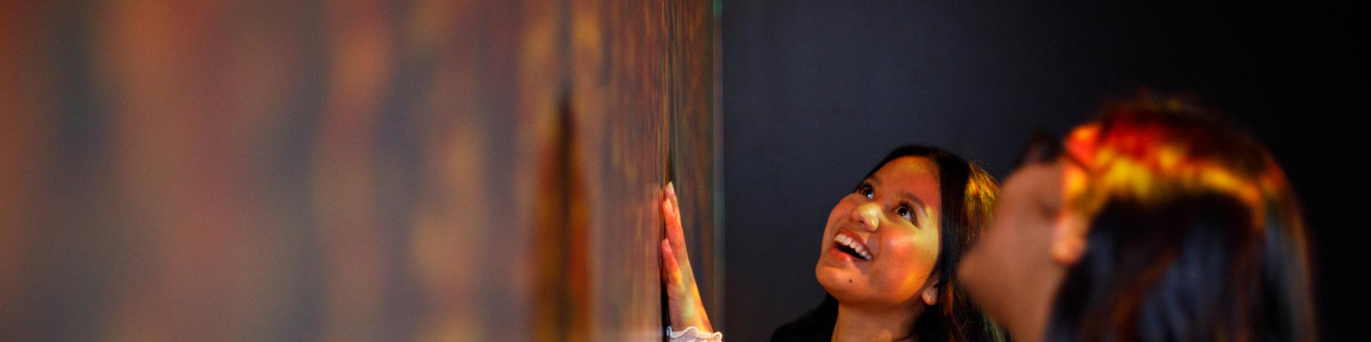 a group of adults are close to a wall of artwork and look up with a happy expression on their faces