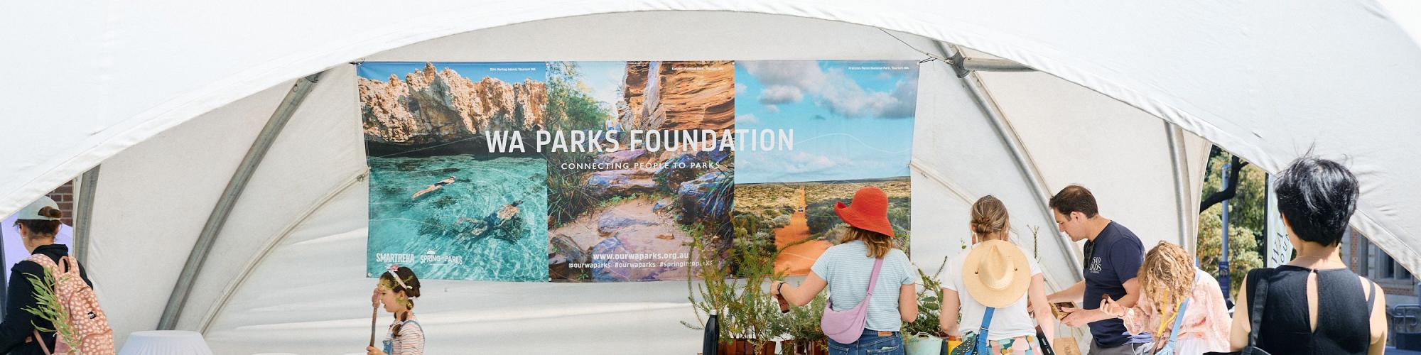 People engaged in outdoor activities under a white tent featuring a "WA Parks Foundation" banner.