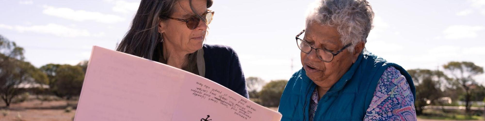 Two people look through a large folio standing in an outback area