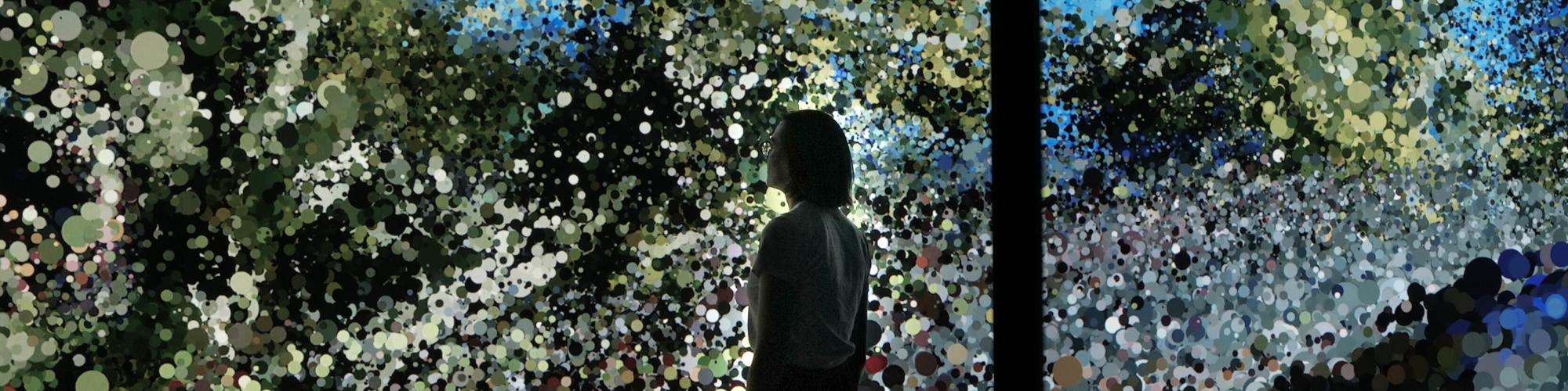 Silhouette of a person looking up at a large screen displaying an artist video of a whale underwater.