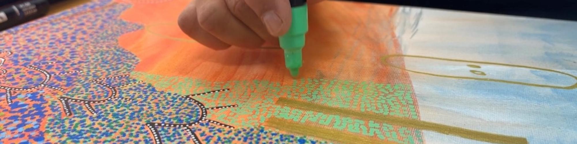 a close up of a colourful artwork and the artists hand adding to the work