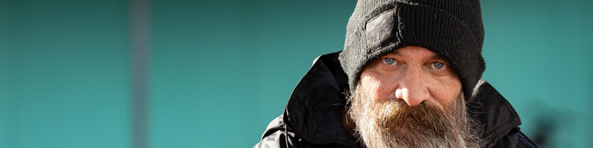 an adult with a beard wearing a beanie stares straight ahead into the camera