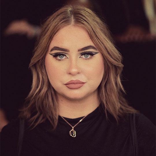 A young woman with dark blonde hair looks seriously at the camera