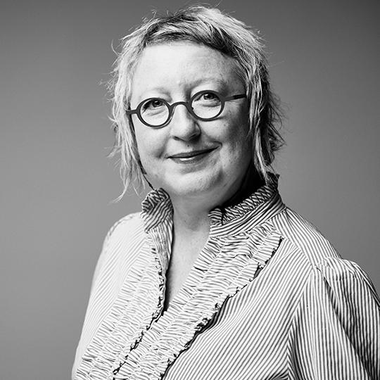 A black and white photograph of a woman with short hair and glasses smiling at the camera