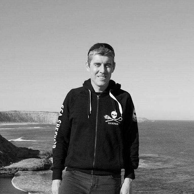 A black and white photograph of a man standing in front of the ocean