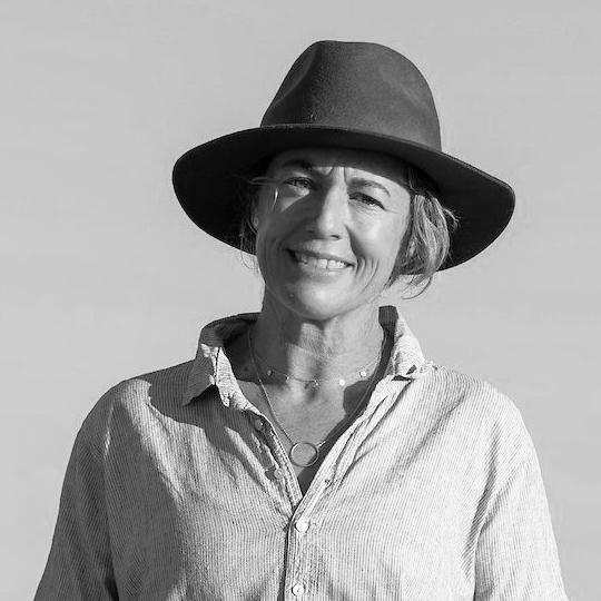 A black and white image of a smiling person wearing a broad-brimmed hat