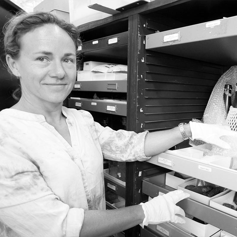 A woman wearing gloves carefully handles collection items in a museum storage area