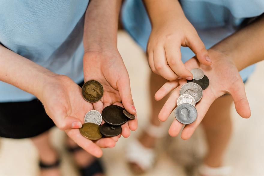 A close-up view of two children's hands holding old coins