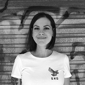 A black and white photo of a woman with short brown hair against a graffiti shed