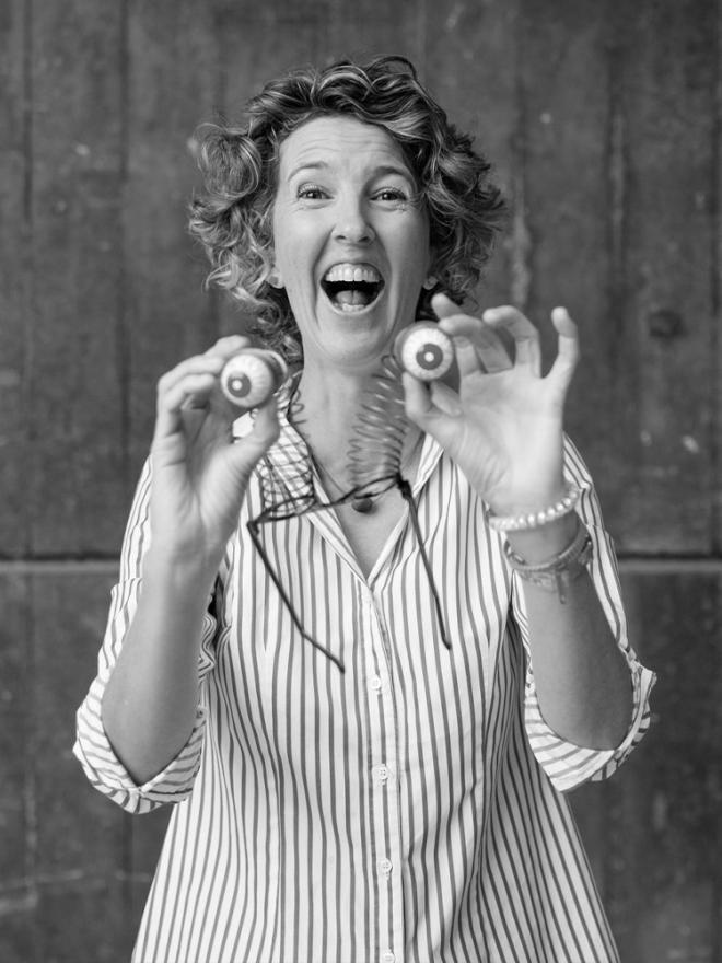 A laughing woman holds two joke eyeballs out towards the camera