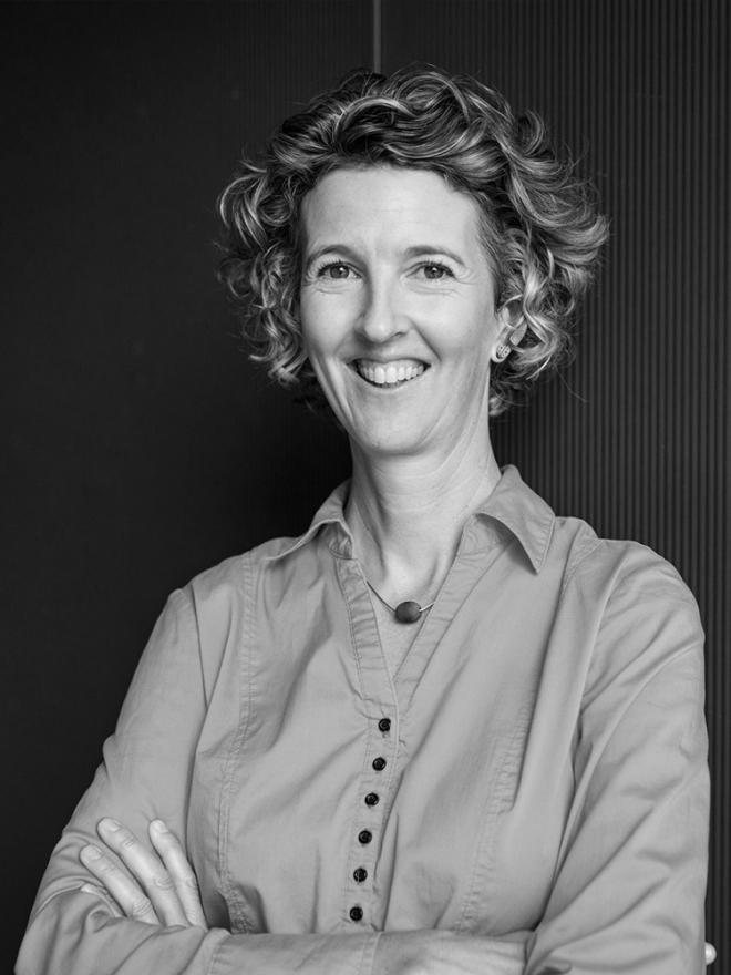 A woman with curly hair crosses her arms and smiles directly at the camera