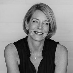 A black and white photo of a women smiling with short blond hair wearing a black top