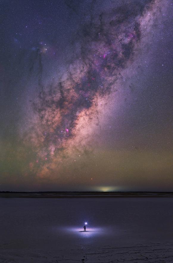 A person stands in an empty landscape beneath a vibrant night's sky