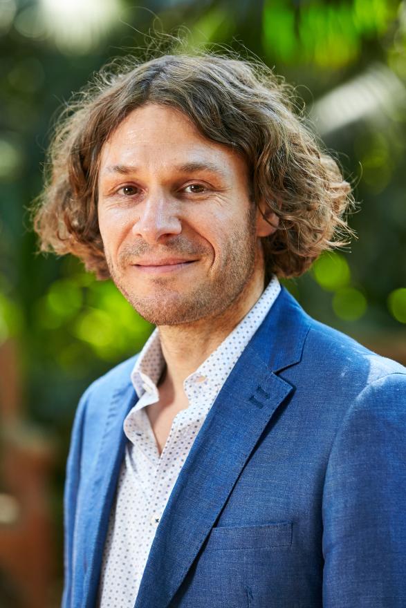 A portrait of a man in a garden wearing a blue suit jacket