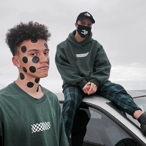 Two young men sit around a parked car under a grey cloudy sky