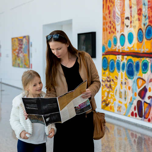 A parent and child stand in a museum gallery looking at a map