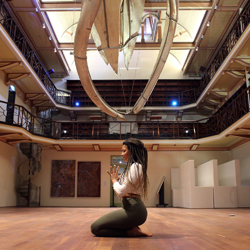 A young woman practices yoga beneath a whale skeleton