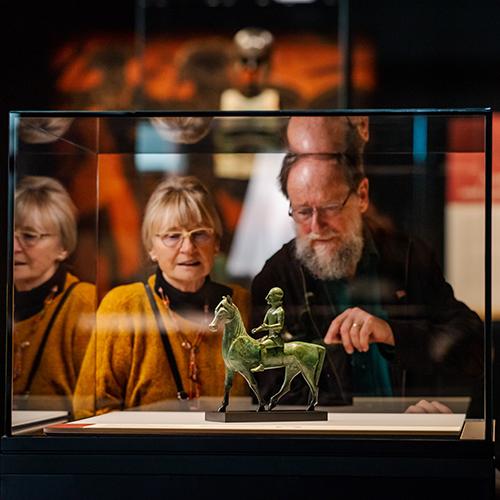 A  man and woman look intently at a small statue in a glass museum showcase