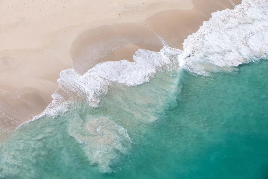 An aerial view of clear turquoise waves breaking on a sandy beach