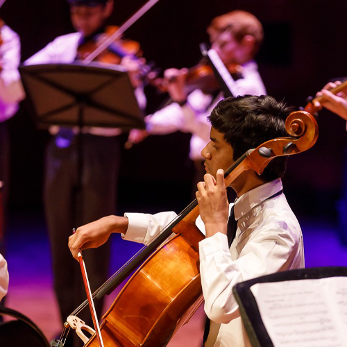 Boys wearing white shirts stand in a circle playing string instruments