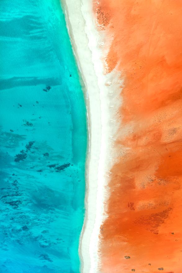 An aerial photograph of bright turquoise water meeting a red sandy landscape