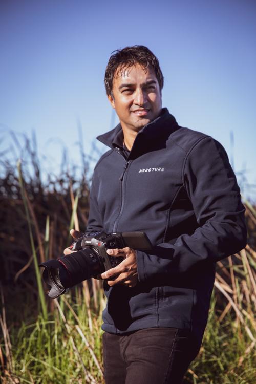 Head shot of Michael Haluwana holding a camera standing in a field with tall grass 