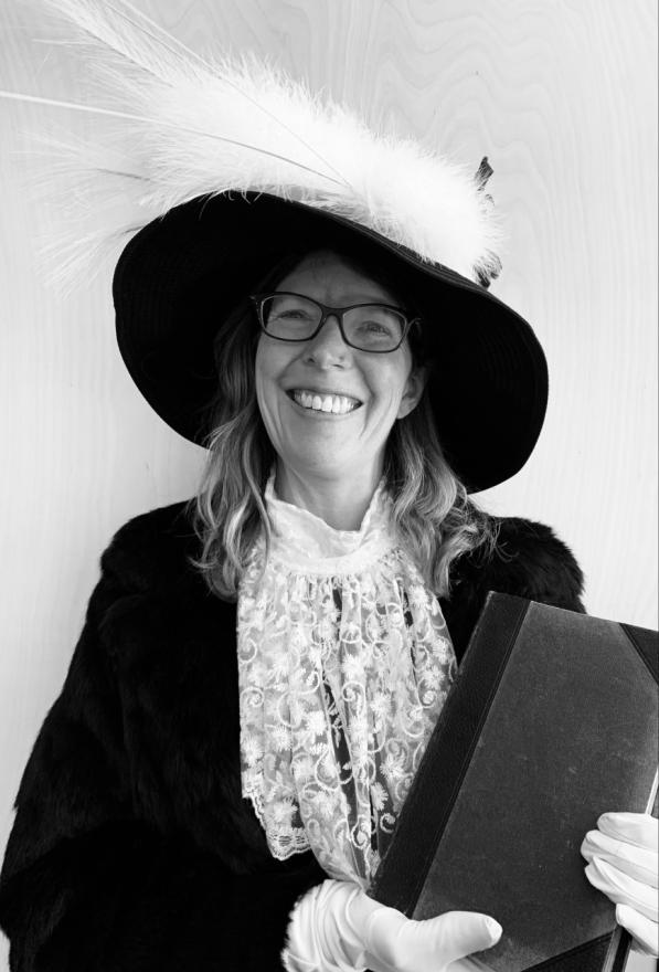 A black and white image of Sandy Barber in costume, wearing a large feathered hat