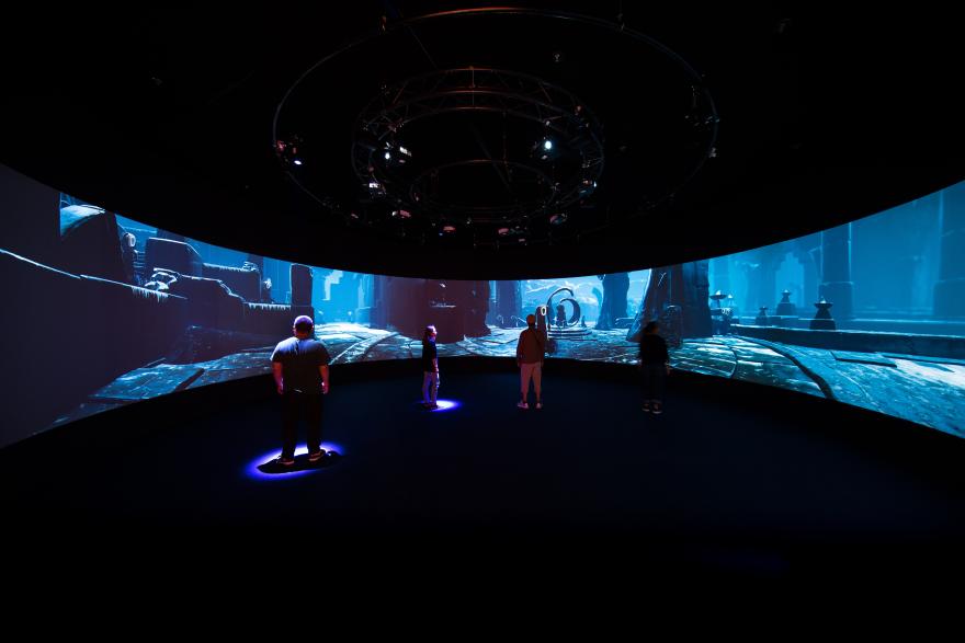 People stand in front of a 180 degree screen displaying an animated fantasy world landscape