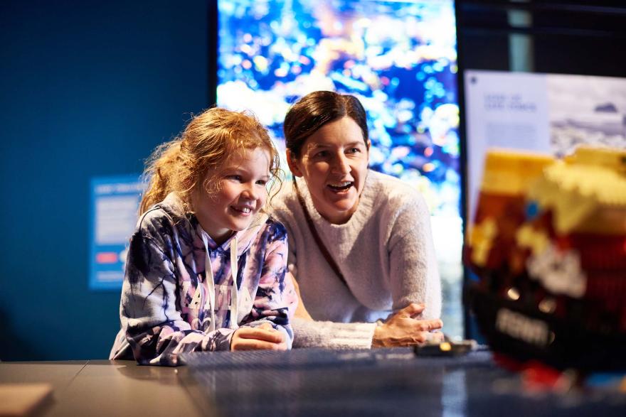 A smiling adult and child look in excitement at a LEGO model of a ship