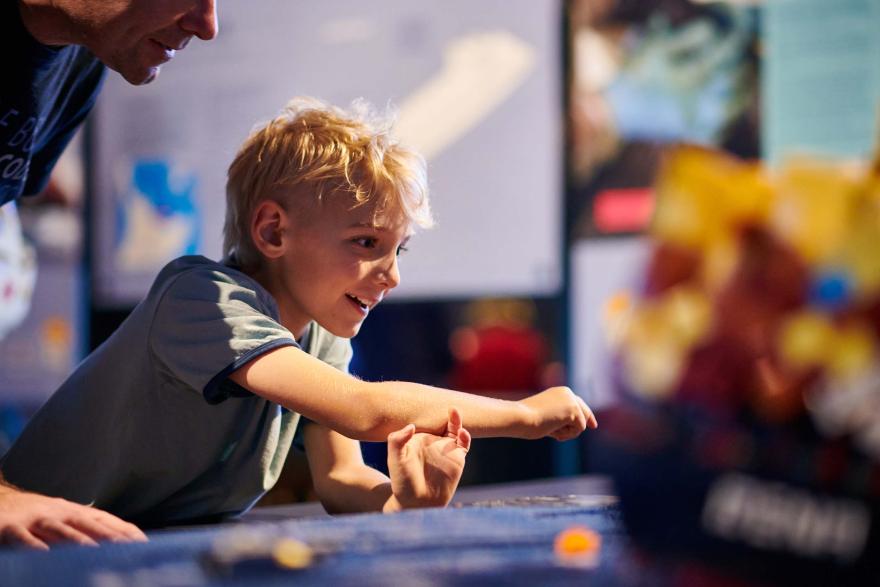 An excited-looking child points towards a LEGO model of a ship