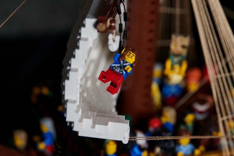 A LEGO minifigure dressed like a 17th century sailor holds onto a rope on a LEGO model of a ship