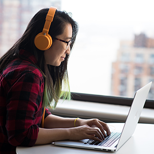A person wearing a pair of orange headphones working at a laptop