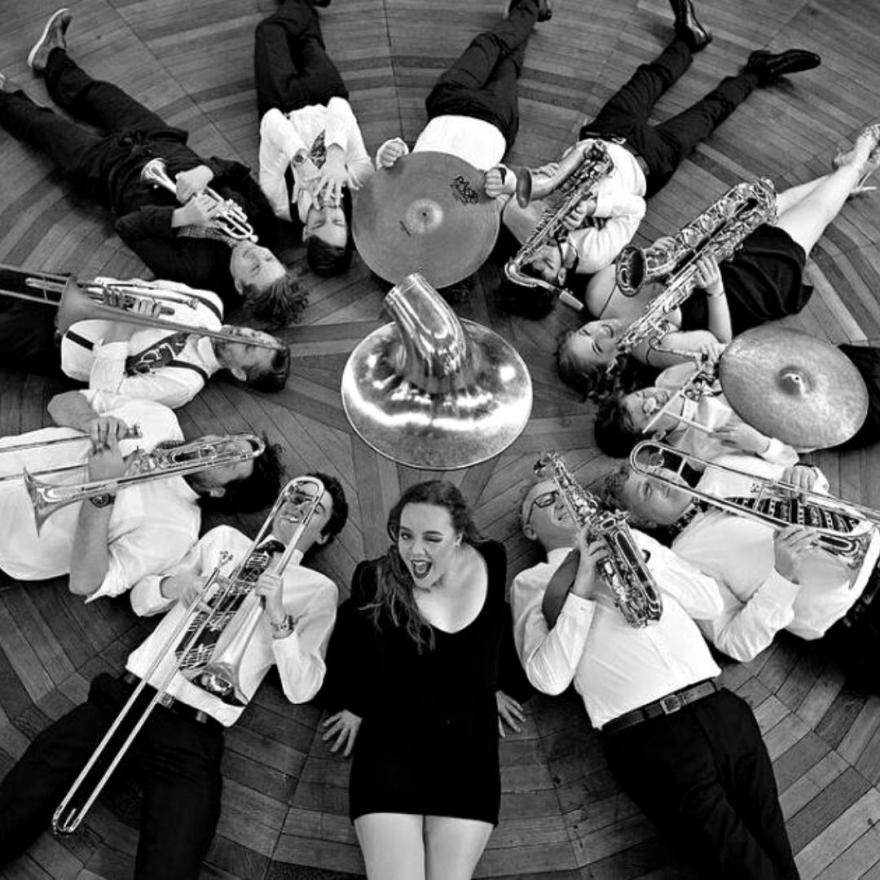 Group of performers holding their instruments lying in a circle with a trumpet in the centre. 